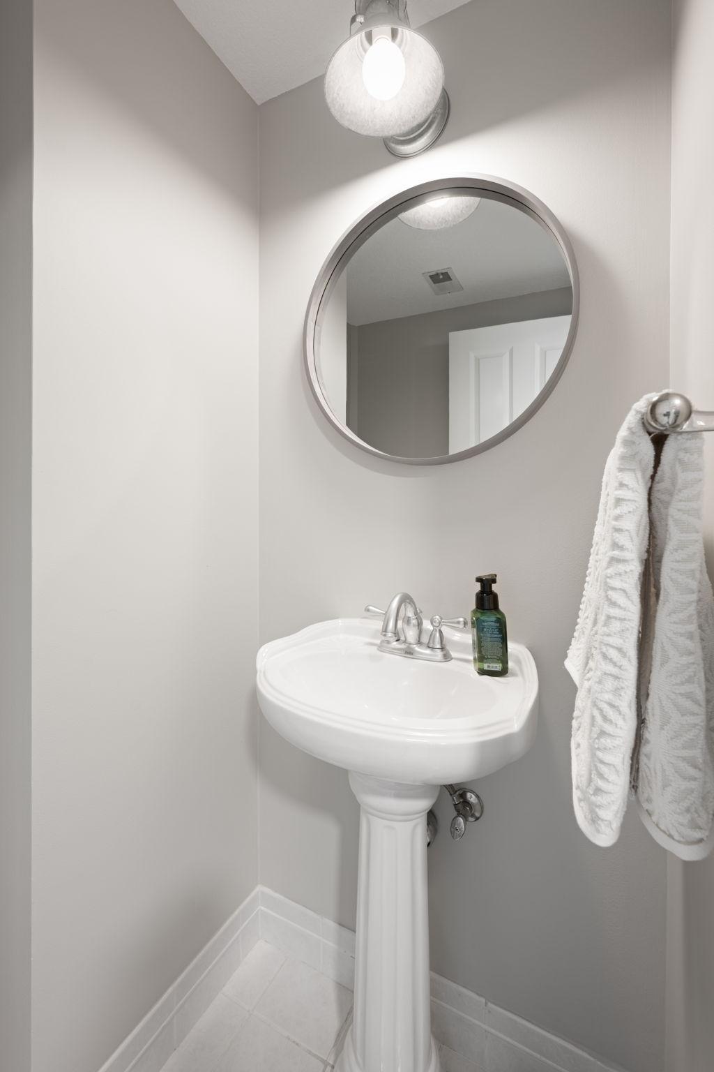 Convenient half bath with pedestal sink, updated mirror, wall sconce lighting, and clean neutral finishes.
