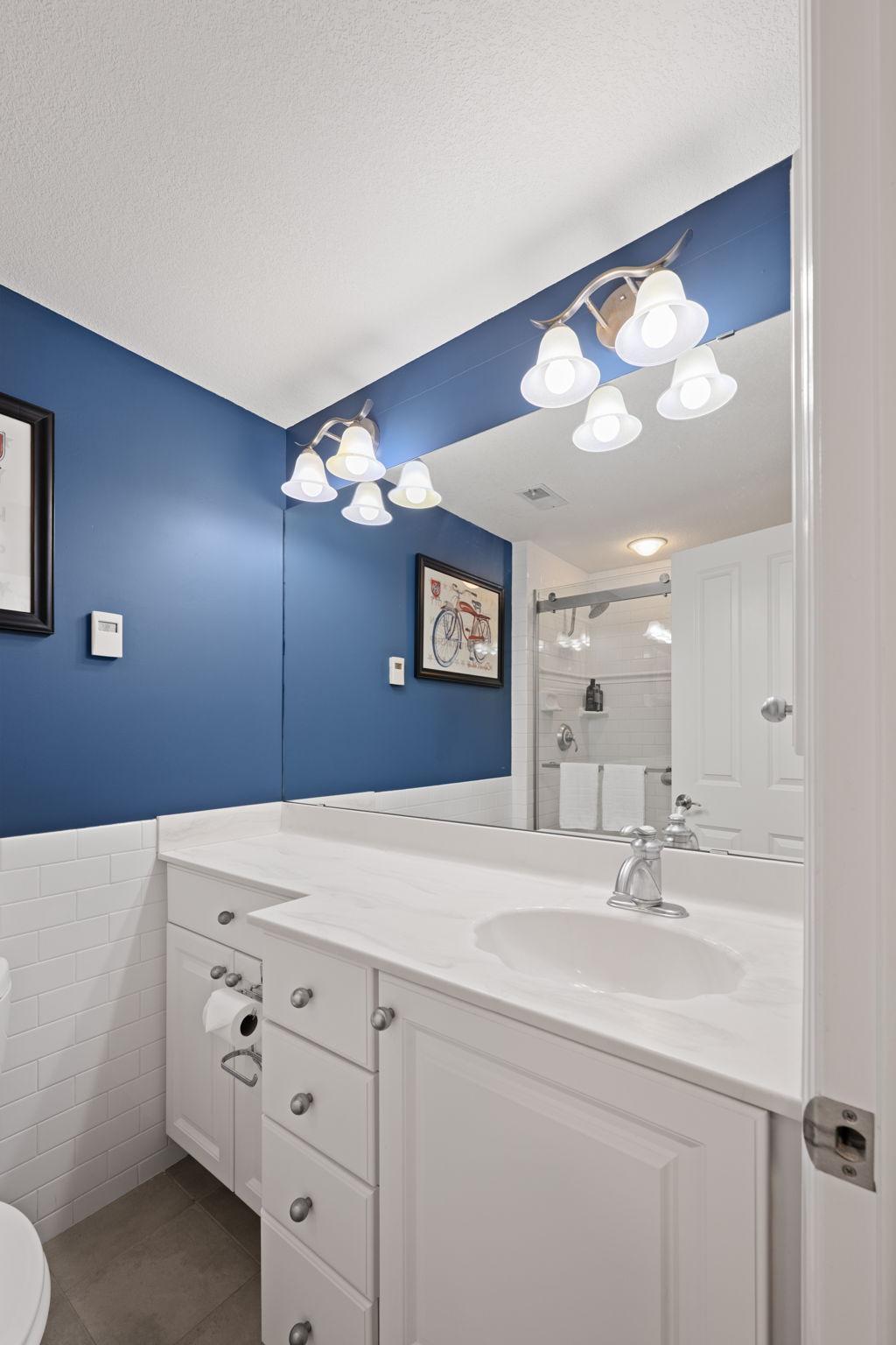 Full bath featuring a white vanity, modern lighting, large mirror, blue accent wall, and clean tile finishes.