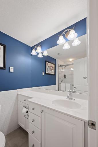 Full bath featuring a white vanity, modern lighting, large mirror, blue accent wall, and clean tile finishes.