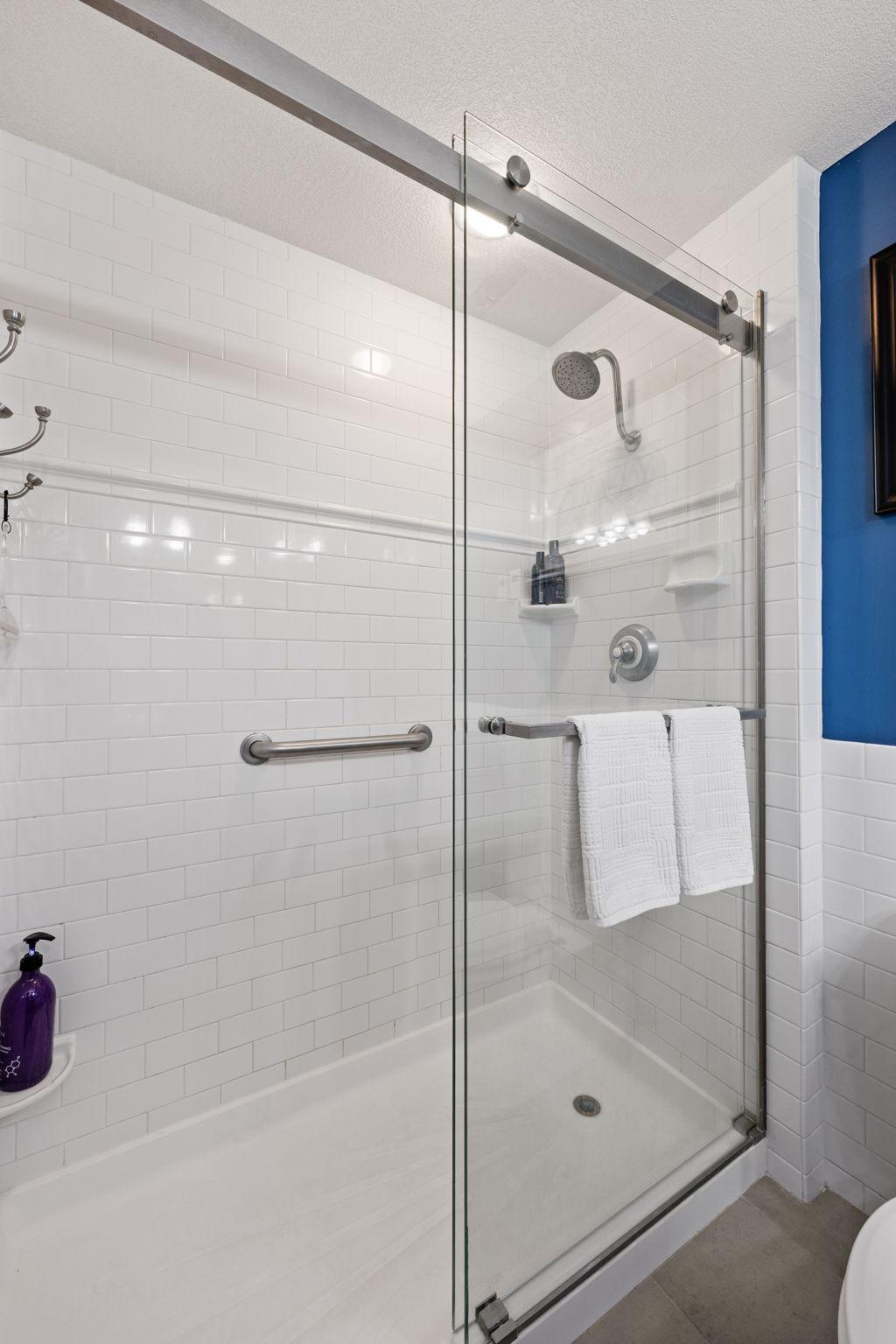 Beautiful tiled walk-in shower with glass sliding door, modern fixtures, built-in shelving, and grab bar.