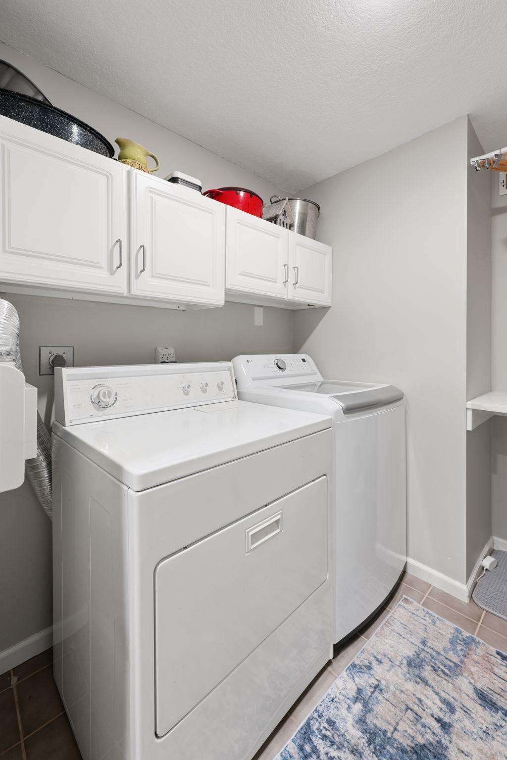 In-unit laundry room with full-size washer and dryer, overhead cabinetry, and additional utility/storage space.