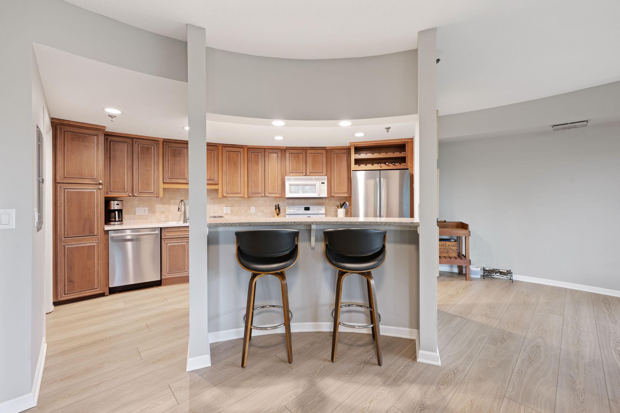 Open kitchen with breakfast bar seating, warm cabinetry, stainless steel appliances, and great connection to the living spaces.