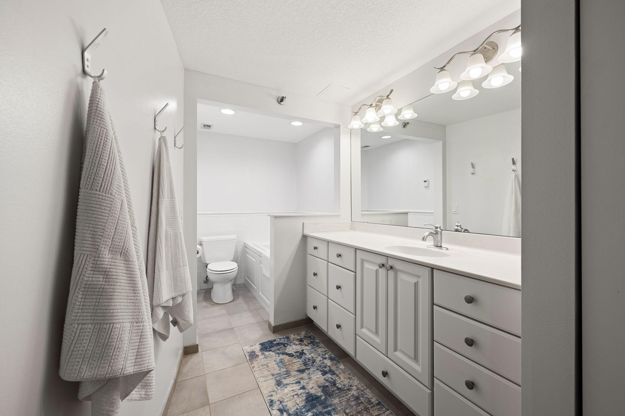 Full primary ensuite bathroom featuring a long vanity, large mirror, modern lighting, tile flooring, and a clean neutral design.