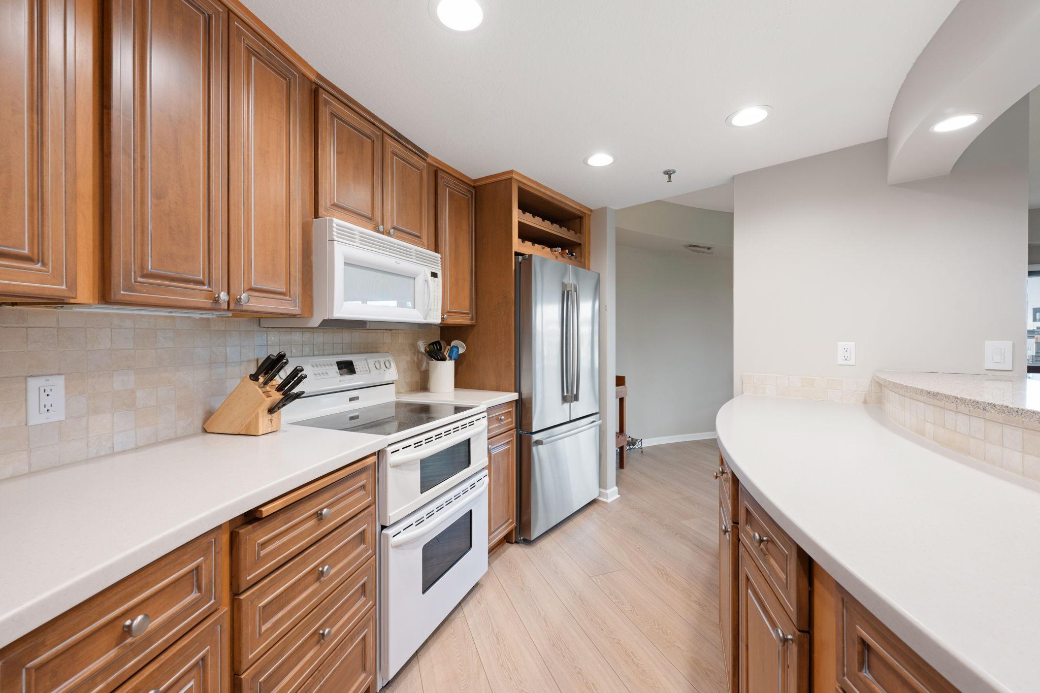 Functional kitchen with excellent cabinet storage, stainless steel refrigerator, breakfast bar, and open sightlines to the main living area.
