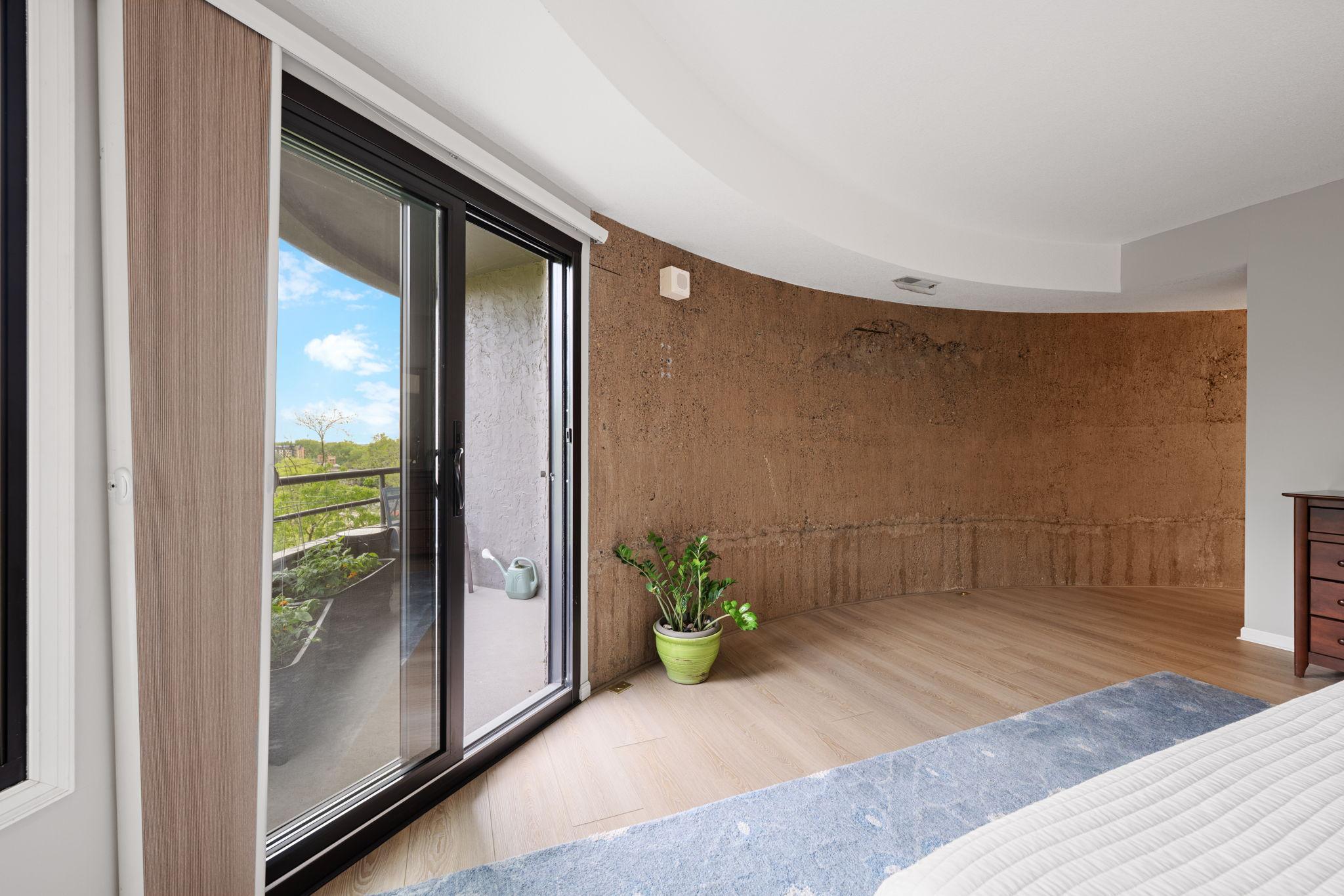 Spacious primary bedroom with direct access to the private balcony, updated flooring, and a distinctive curved architectural accent wall.