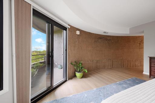 Spacious primary bedroom with direct access to the private balcony, updated flooring, and a distinctive curved architectural accent wall.