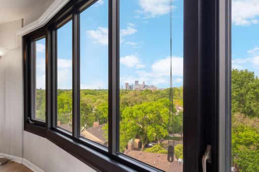 Expansive windows showcase stunning city skyline views, mature trees, and abundant natural light throughout the unit.