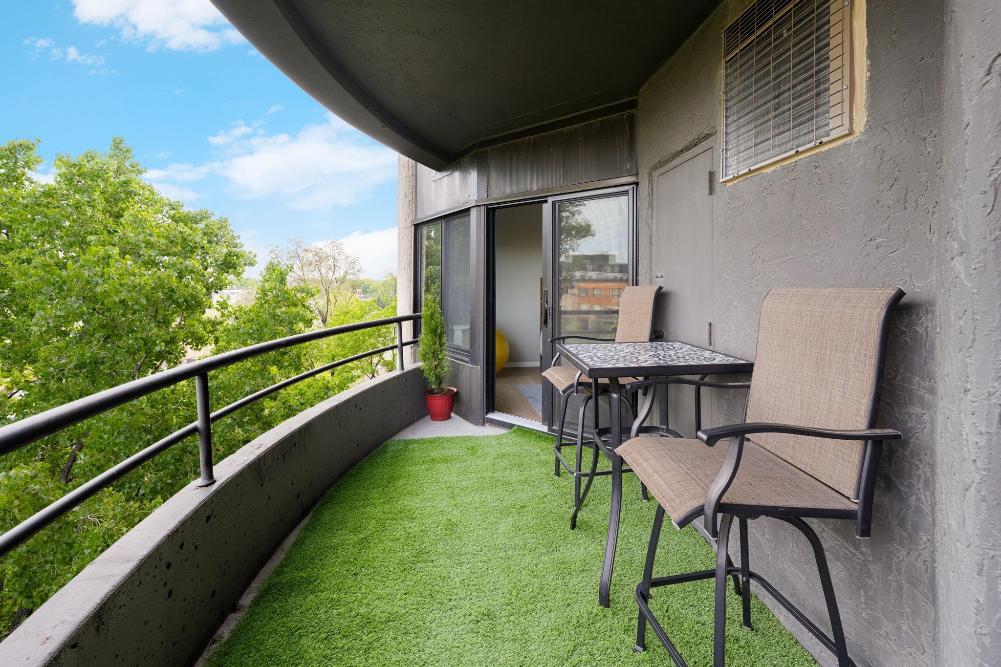 Spacious private balcony with room for outdoor dining or lounge seating, surrounded by mature trees and city views.