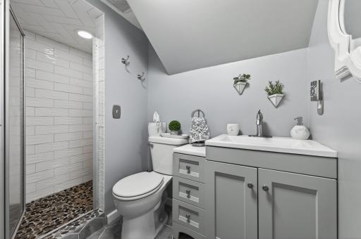 The sellers' favorite bathroom in the house â renovated with a pebble mosaic shower floor, subway tile walk-in shower with glass door, gray shaker vanity, and modern fixtures.