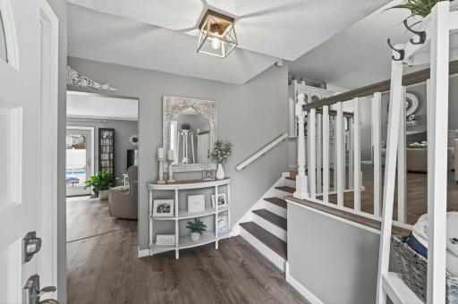 Light-filled entry level foyer with updated LVP flooring, stylish geometric pendant light, and a staircase with refinished treads and freshly painted white spindles.