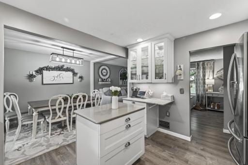 Wide view of the renovated kitchen open to the dining room â white shaker cabinets, quartz countertops, stainless appliances, and natural light from multiple directions.