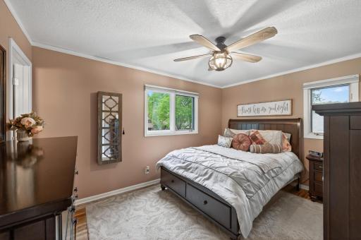 The upper-level primary suite features warm tones, ceiling fan, two windows with tree views, crown molding, and direct access to the private Â¾ bath.