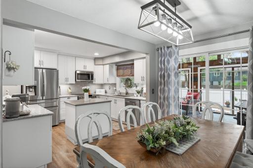 The dining area bridges the living room and kitchen with room for a full table, a statement cage pendant overhead, and a slider opening directly to the three-season porch.