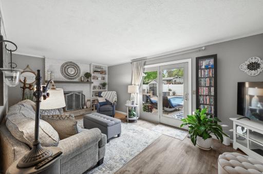 The brick fireplace anchors this entry-level family room â painted white surround, built-in shelving, and French doors looking out to the patio and pool beyond.