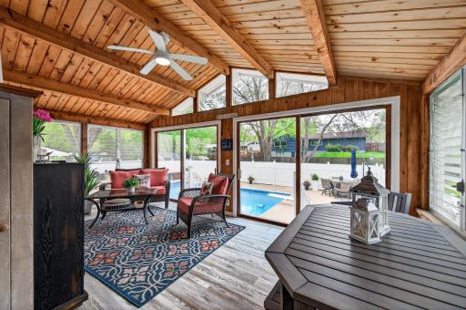 Accessed directly from the dining room, the three-season porch features a vaulted knotty pine ceiling with exposed beams, ceiling fan, large windows on three sides, and a direct view of the pool.