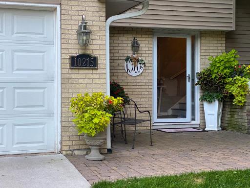 Charming paver courtyard entry with address plaque, coach lighting, and colorful planters â a warm first impression that sets the tone for everything inside.