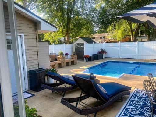 The private stone paver patio with fire table and bistro seating sits just off the pool â surrounded by the vinyl fence with mature trees overhead. A perfect end to a summer evening.