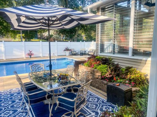 The back of the home shows the full outdoor picture â three-season porch, dining room slider, stamped concrete patio, and the pool all working together seamlessly.
