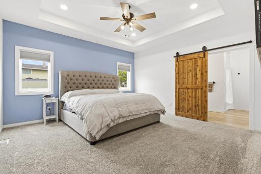 Welcome to the primary suite - the tray ceiling adds depth and volume to the space while the custom barn door to the private ensuite adds a pop of contrast