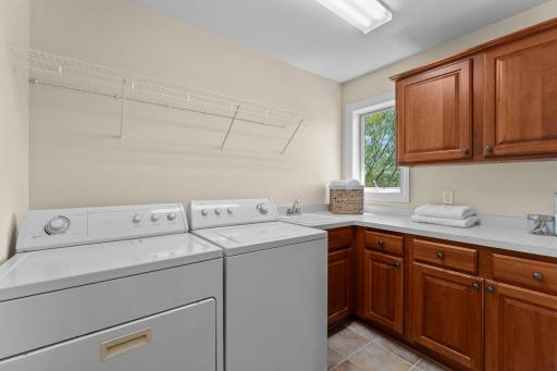 The convenient main level laundry room features tile flooring, ample cabinetry, generous counter space, and a utility sink.