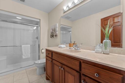 A nearby three-quarter bathroom includes tile flooring, a single vanity, and a walk-in shower.