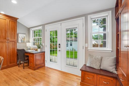 Beautiful French doors are flanked by a built-in desk to the left and a bench to the right, complete with spacious wall storage for daily essentials. The doors open to a lovely paver patio overlooking the fenced backyard and two-car garage
