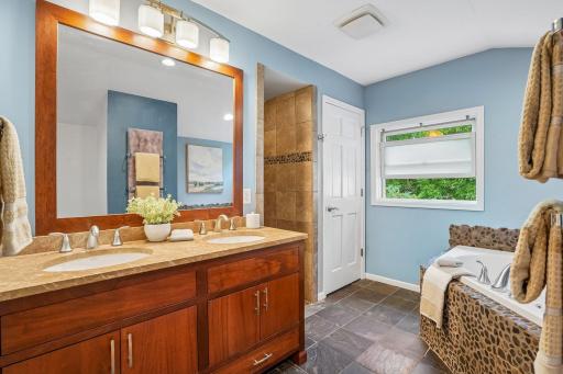 The primary bath sits just off the bedroom area, beautifully appointed with natural stone, a spacious double vanity, a whirlpool tub, and a separate large walk-in shower