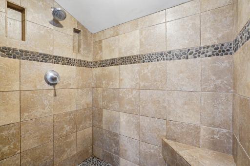 The large walk-in shower features beautiful stone trim that elegantly complements the design of the whirlpool bath