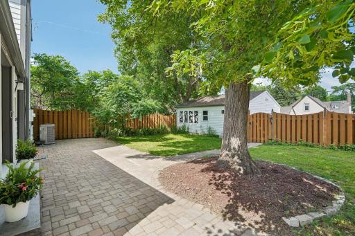 The lovely back yard is fully fenced with a generous paver patio, framed by mature trees, offering a private, shaded oasis perfect for outdoor relaxation and recreation