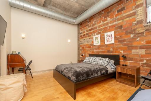 Spacious primary bedroom #1 continues with the authentic loft vibe with concrete ceilings, exposed ductwork, and an exposed brick feature wall