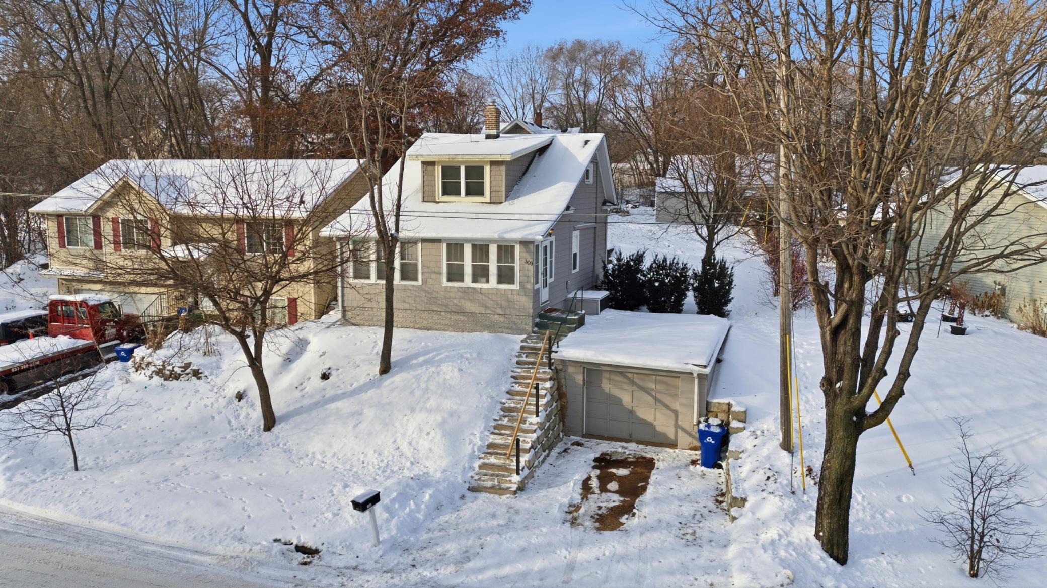 Front of home with one stall attached garage that leads into the unfinished basement. Sellers had the exterior stairs redone and installed a retaining wall behind where the garbage cans sit.