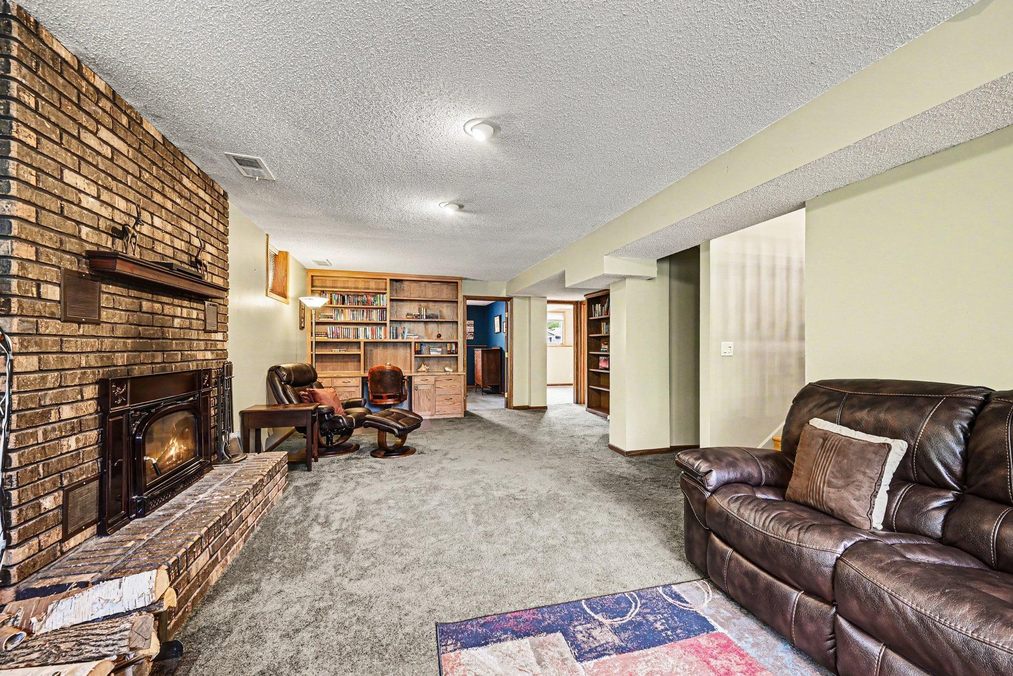 “The lower-level family room offers a cozy wood-burning fireplace, perfect for Minnesota evenings.” Built in Bookcase and desk made of natural wood, stay with the home