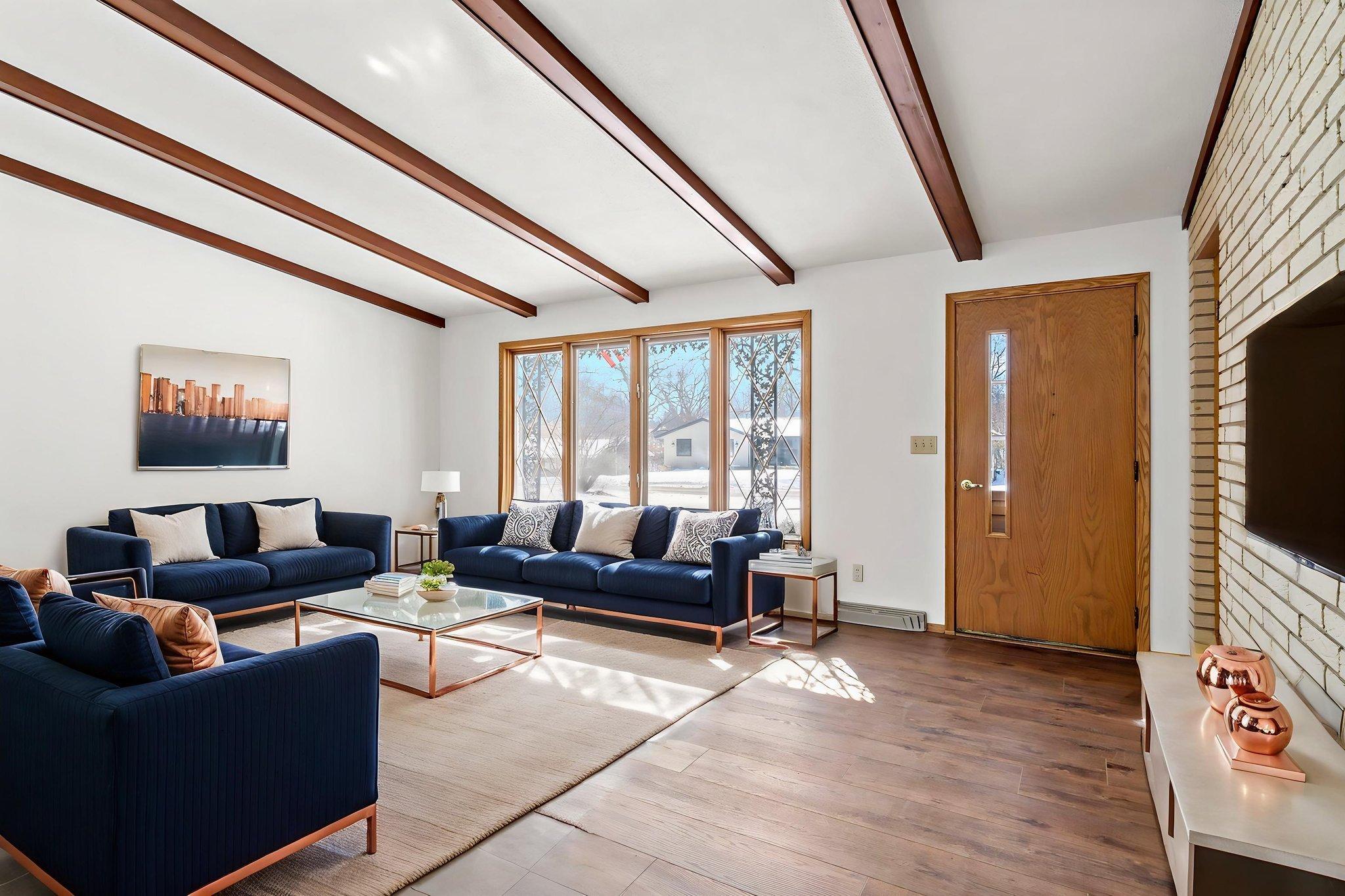 Main level living room with ceiling beams and brick feature wall. Photo is virtually staged.