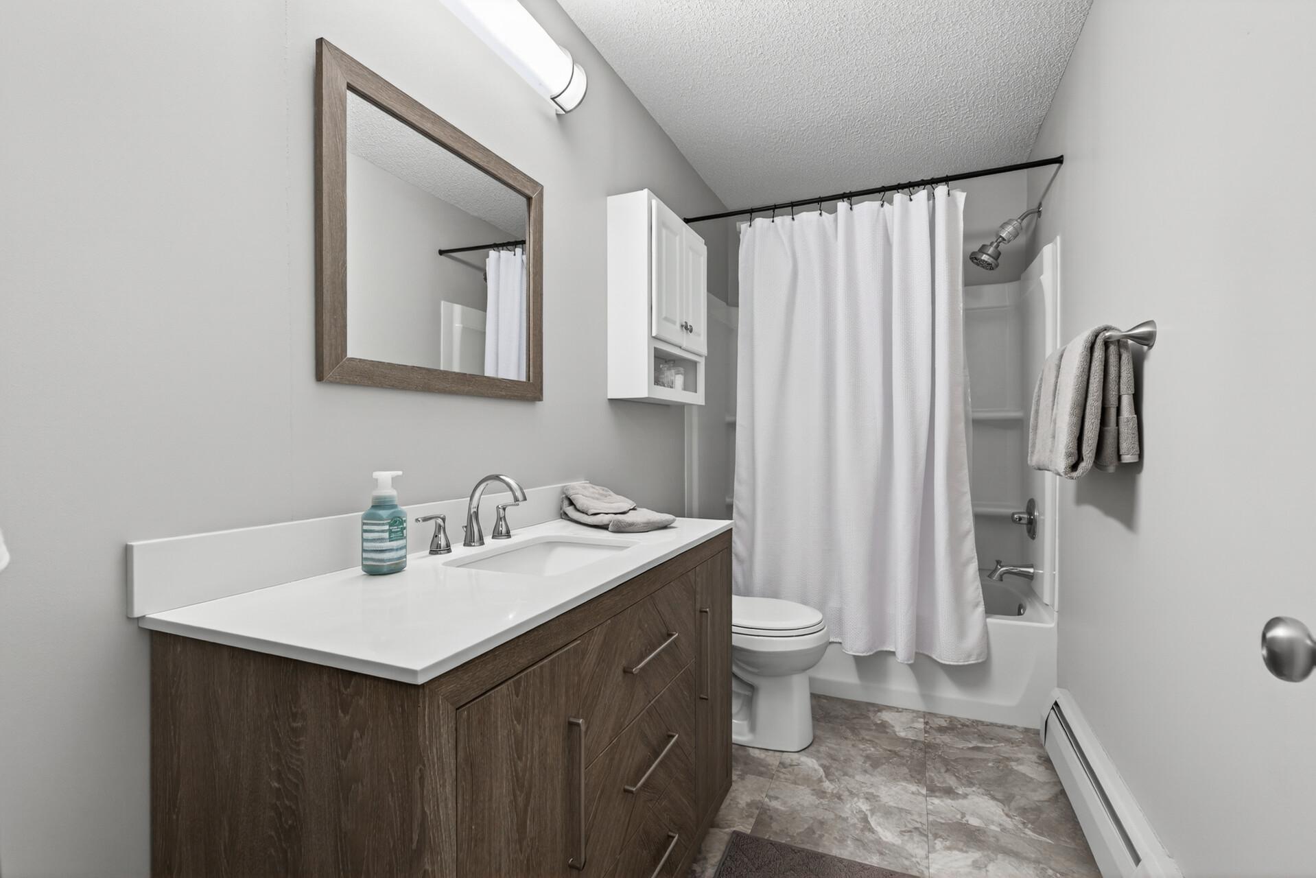 Updated full bath with a clean neutral style, generous vanity storage, and a nearby tall linen closet for extra towels and essentials.