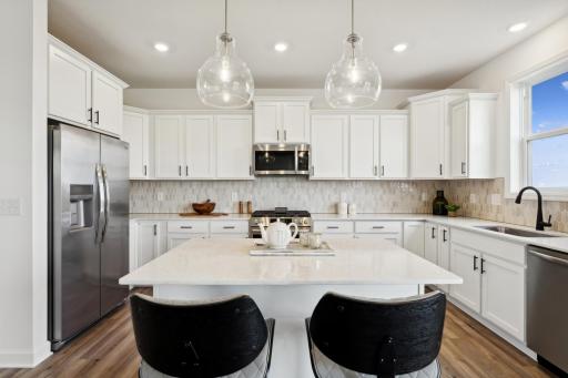 (Photo of a decorated model, actual homes finishes will vary) This stunning kitchen features a large center island, quartz countertops, LVP floors, stainless steel appliances, and more!