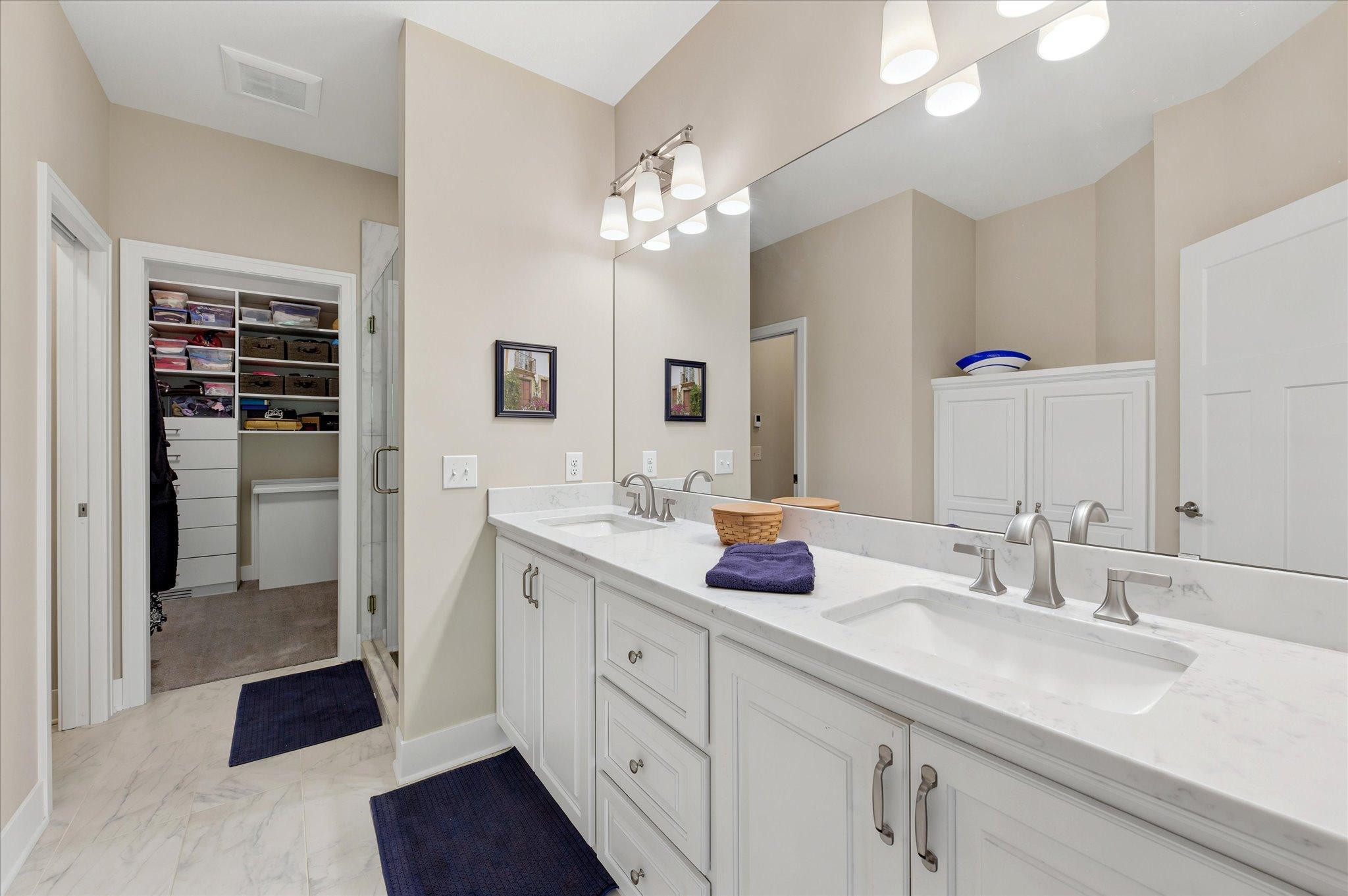 Primary bath with a double sink vanity, built-in linen cabinet, walk-in closet with access cabinet to the main floor laundry room, jewelry drawers, and organizers-