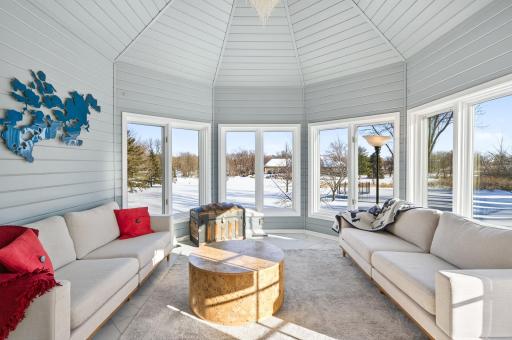 The sunroom is filled with natural light and showcases marble flooring, glass French doors, walls of windows, and a beautiful chandelier, creating an inviting space to relax or entertain.