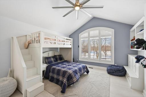 Bedroom two features a vaulted ceiling, modern ceiling fan, luxury plank flooring, large window, built-in shelving, and a spacious with built-ins.