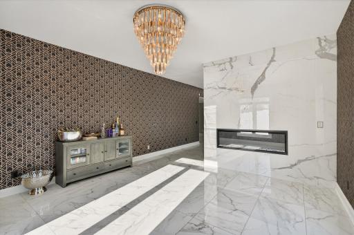The sitting area shares the double-sided fireplace and offers marble floors, a statement chandelier, and large windows that flood the space with natural light.