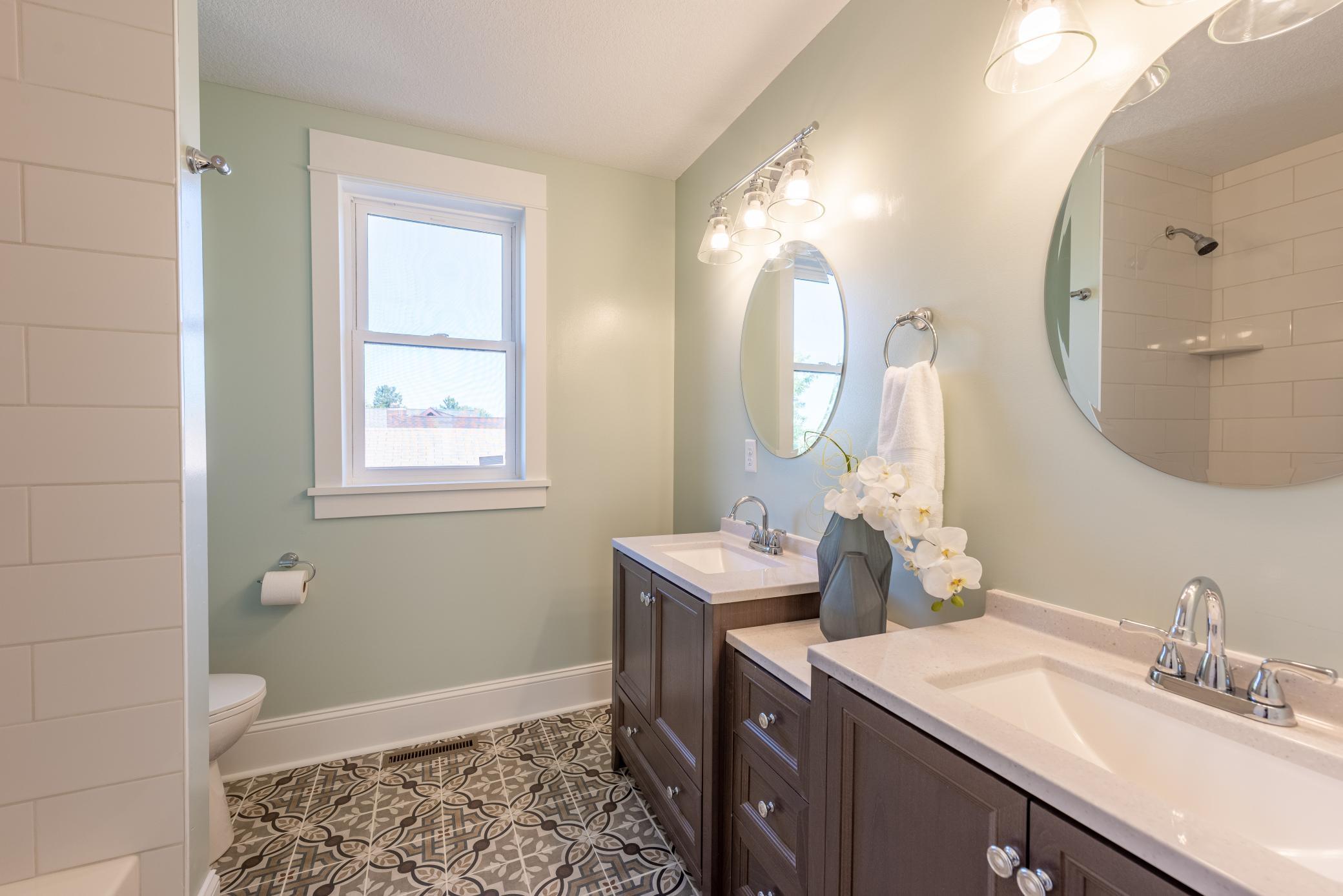 Double vanities with patterned tile floor and bathtub with tile surround to the ceiling