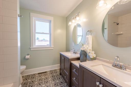 Double vanities with patterned tile floor and bathtub with tile surround to the ceiling