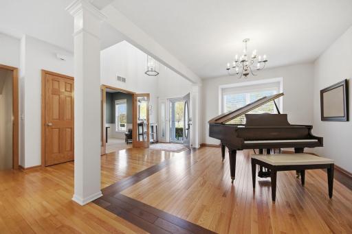 The music room features immaculate oak floors bordered by rich Brazilian walnut trim, creating a warm and sophisticated ambiance beneath a beautiful chandelier. It could easily be reimagined as a formal dining room.