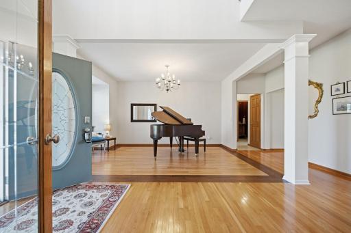The music room features immaculate oak floors bordered by rich Brazilian walnut trim, creating a warm and sophisticated ambiance beneath a beautiful chandelier. It could easily be reimagined as a formal dining room.