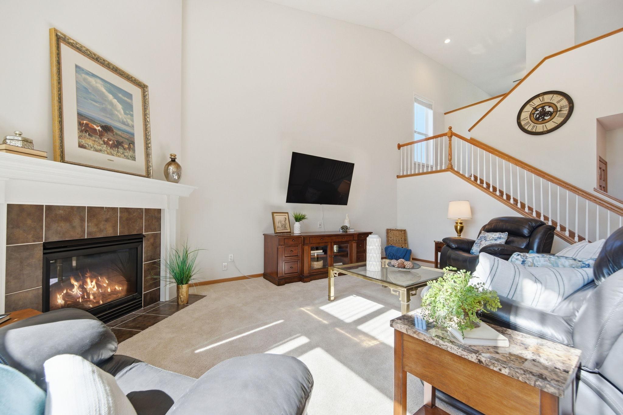 A stunning main-floor family room features soaring vaulted ceilings, a ceiling fan, cozy gas fireplace, and luxurious plush carpeting. Exceptionally spacious and bathed in natural light, this inviting room is ideal for both relaxing and entertaining.
