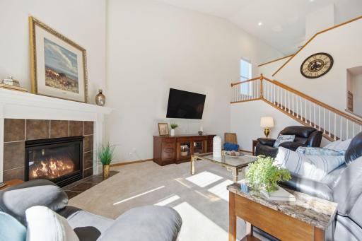 A stunning main-floor family room features soaring vaulted ceilings, a ceiling fan, cozy gas fireplace, and luxurious plush carpeting. Exceptionally spacious and bathed in natural light, this inviting room is ideal for both relaxing and entertaining.