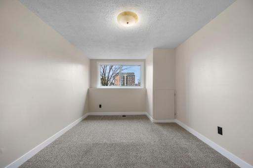 Bright and versatile room with neutral finishes, soft carpeting, and a large window offering natural light and neighborhood views.
