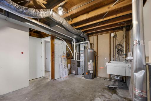 Utility and mechanical room featuring furnace, water heater, and laundry sink, with exposed beams and ample space for storage.