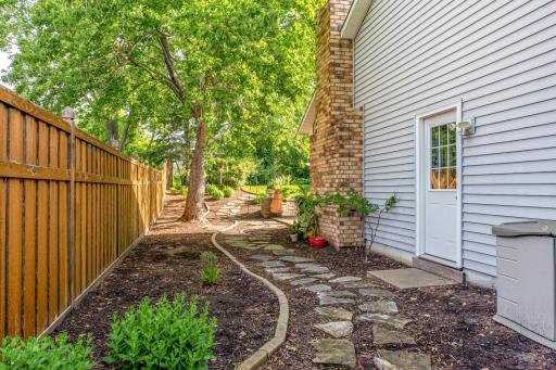 A convenient side yard features a decorative stone pathway, mature shade trees, and easy access to the backyard with plenty of space for gardening.