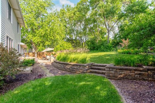 Terraced landscaping, lush green space, and mature trees create a private backyard retreat with year-round beauty.