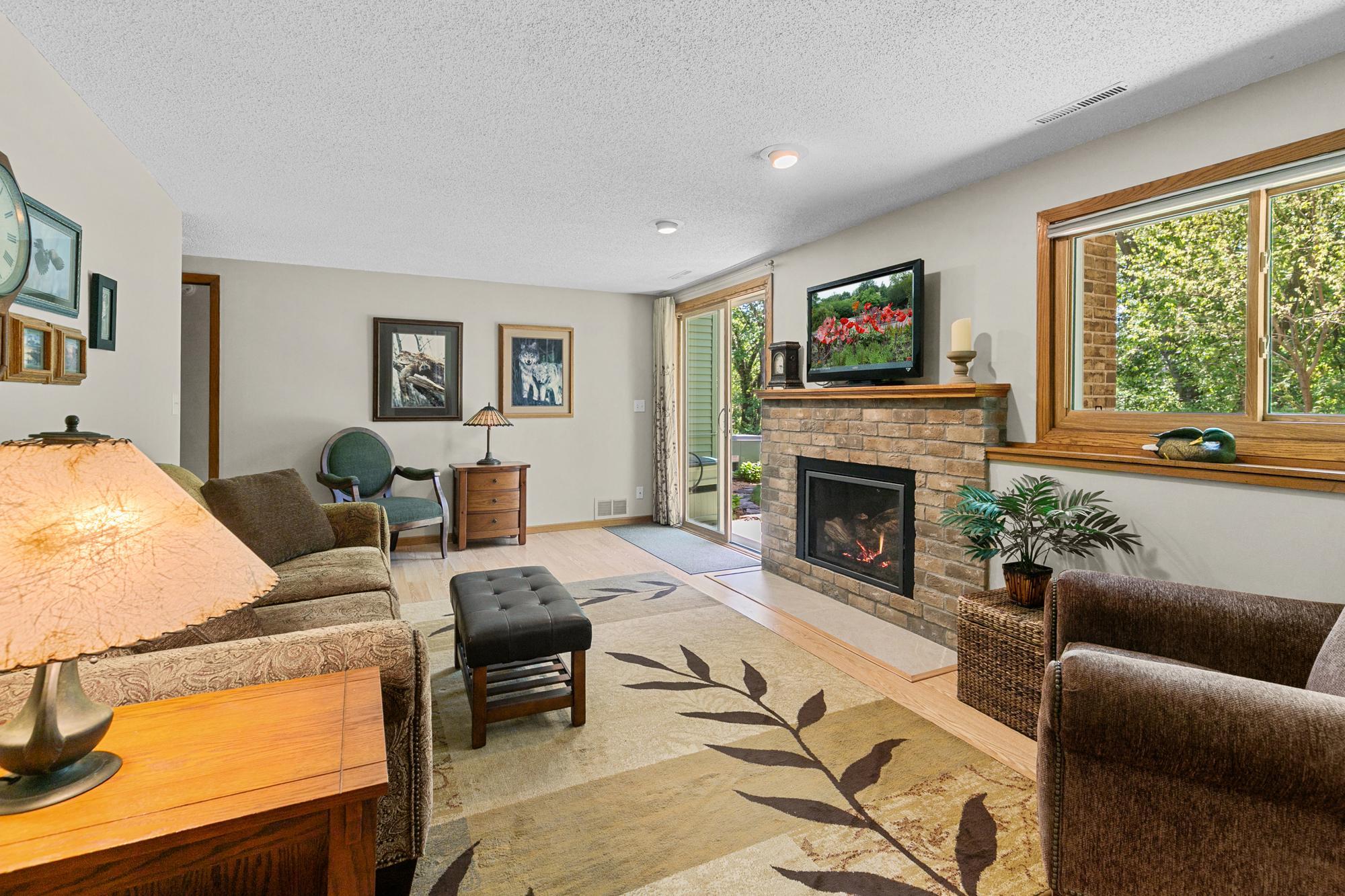 Lower-Level family room appointed with another gas burning fireplace with brick surround and tasteful mantle. Walk-Out lower level is home to nature inspired views, patio, and family gathering space - witness to it all.